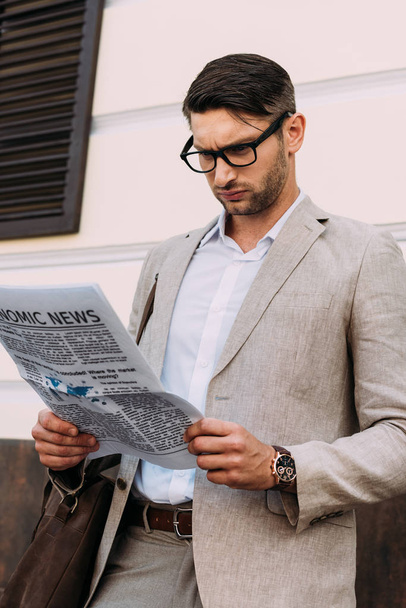 συγκεντρωμένος επιχειρηματίας σε γυαλιά διαβάζοντας εφημερίδα στο δρόμο - Φωτογραφία, εικόνα