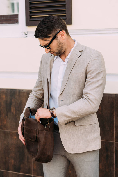 serious businessman in wristwatch holding leather bag on street - Zdjęcie, obraz