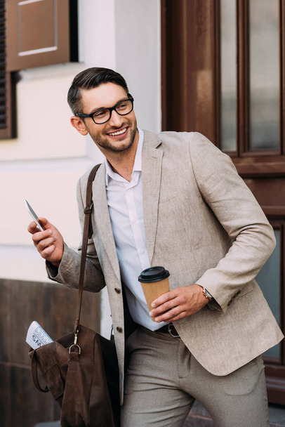 усміхнений бізнесмен в окулярах тримає смартфон і каву, щоб вийти на вулицю
 - Фото, зображення