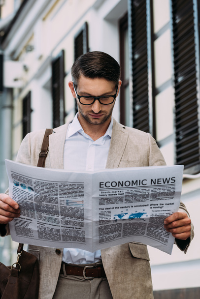 front view of concentrated man in glasses reading newspaper on street - Foto, imagen