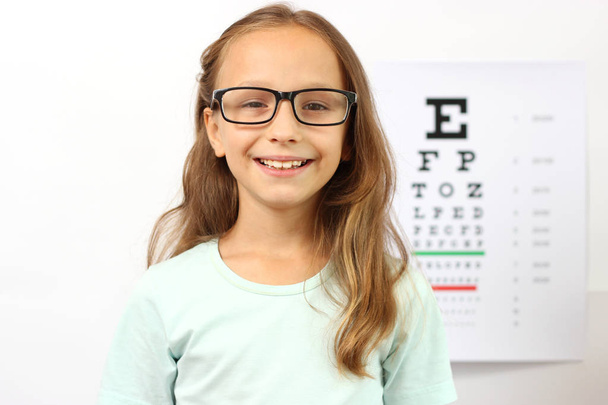 маленькая симпатичная жизнерадостная девочка проходит глазной тест в кабинете офтальмолога - Фото, изображение