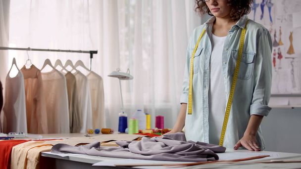 Dressmaker unfolding cloth on work table and attaching patterns, fashion design - Фото, зображення