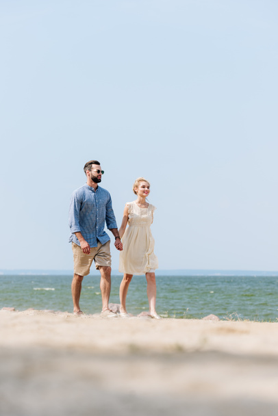ビーチに沿って歩いて手をつないでいる大人のカップルの選択的な焦点 - 写真・画像