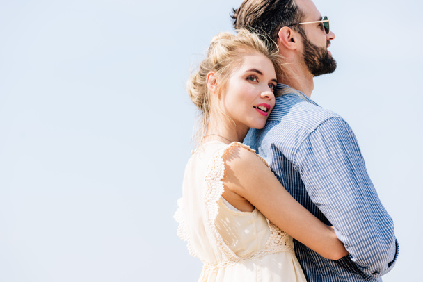 young beautiful blonde woman hugging bearded boyfriend with clear sky on background - Фото, зображення