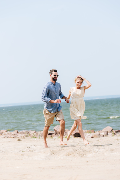 happy young couple holding hands while running along beach - Фото, зображення