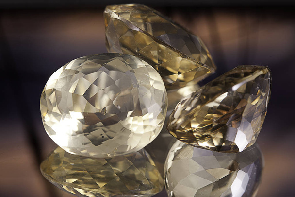 Группа больших белых и желтых прозрачных камней в форме алмаза на отражающей поверхности с цветами заката на заднем плане
 - Фото, изображение