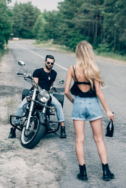 vissza véve a lány sétált úton egy üveg alkohollal közel jóképű barátja napszemüveg a fekete motorkerékpár - Fotó, kép