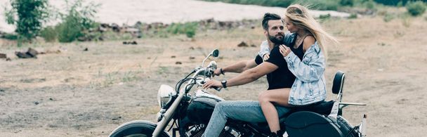 jovem casal de motociclistas abraçando na motocicleta preta na praia de areia perto do rio, tiro panorâmico
 - Foto, Imagem