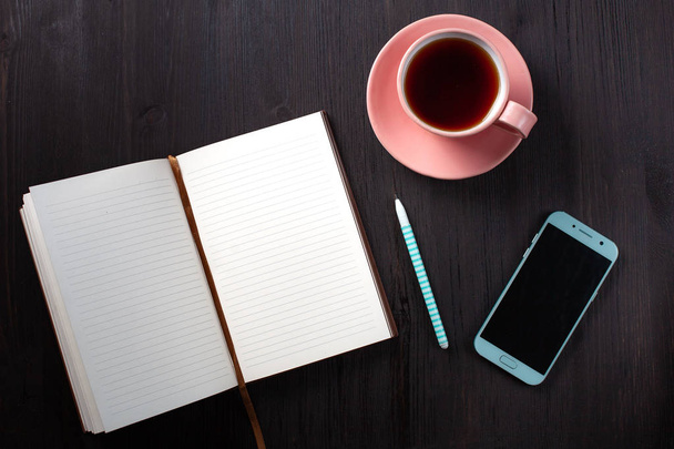 Opened notebook, cup of tea, pen, phone on  black background - Foto, imagen