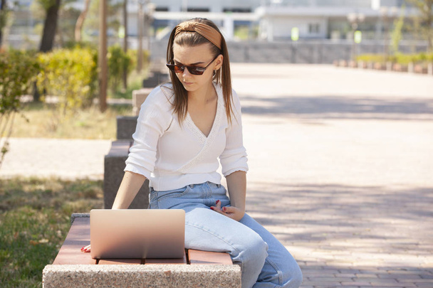Beautiful woman sitting on a park bench using a laptop. - Foto, afbeelding