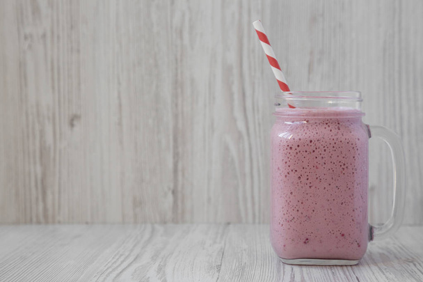 Strawberry banana smoothie in a glass jar over white wooden back - Zdjęcie, obraz