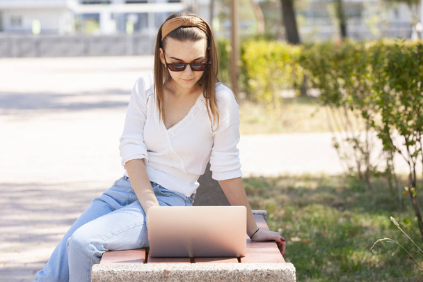Beautiful woman sitting on a park bench using a laptop. - Fotó, kép