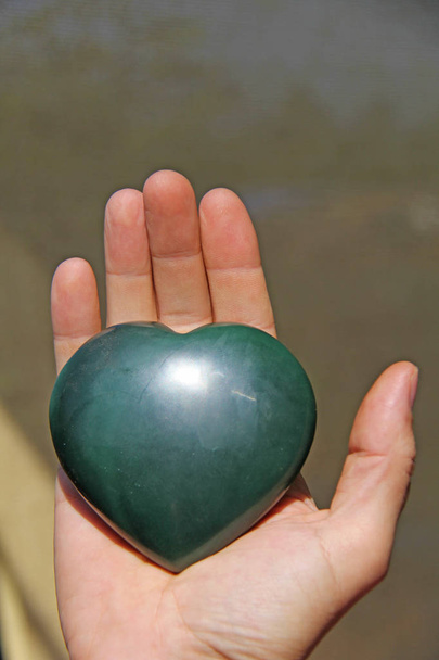 De hand houdt het hart van natuurlijke steen groene jade. Hart in - Foto, afbeelding