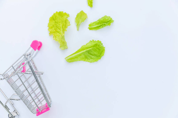 Carrinho de supermercado pequeno empurrar supermercado para fazer compras com folhas de alface verde isolado no fundo branco
 - Foto, Imagem