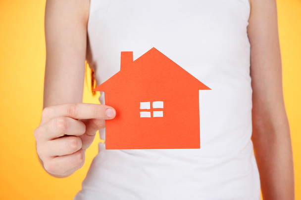 papier huis in handen op oranje achtergrond - Foto, afbeelding