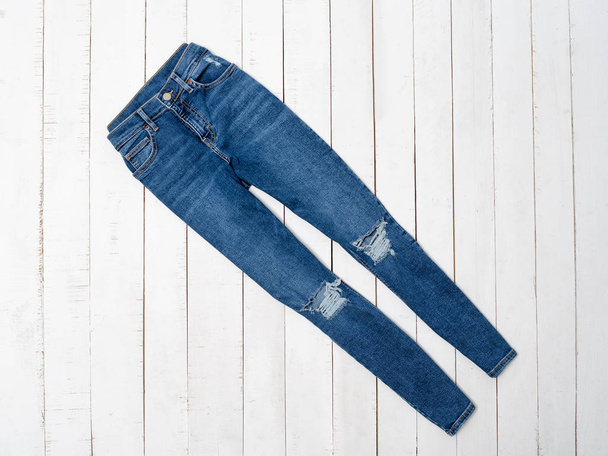 Blue ragged jeans on a white wooden background. Clothing concept. Flat lay - Photo, Image