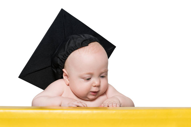 Um bebé curioso com chapéu académico à mesa. Conceito educacional. Isolar
 - Foto, Imagem