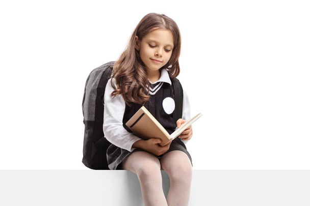 Schoolgirl ina üniforma bir panelde oturan ve bir kitap okuma  - Fotoğraf, Görsel