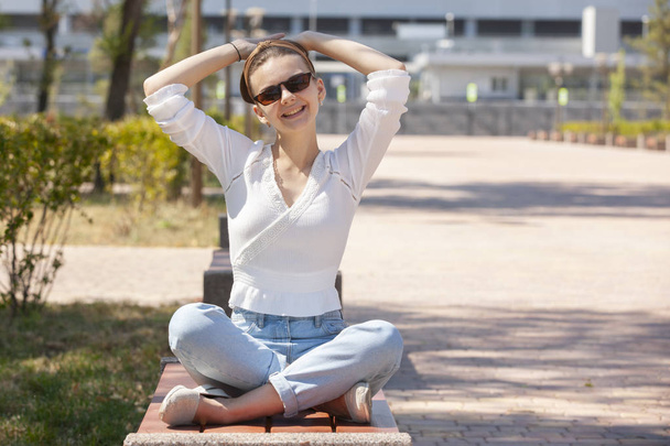 Jonge mooie vrouw zittend op een bankje in het park. - Foto, afbeelding