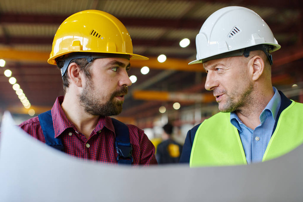 Engineers in hard hats look at each other while holding a blueprint. - Foto, Imagem