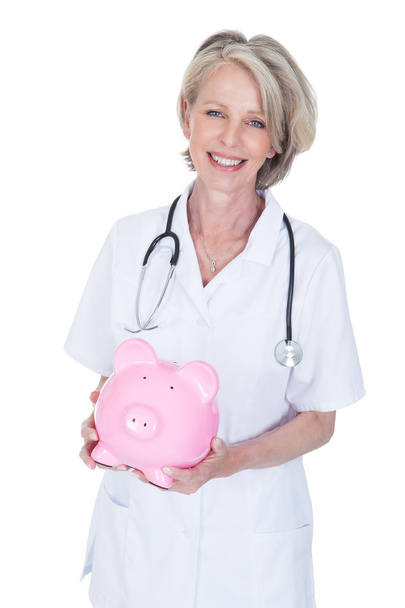 Mature Female Doctor Holding Piggybank - Φωτογραφία, εικόνα