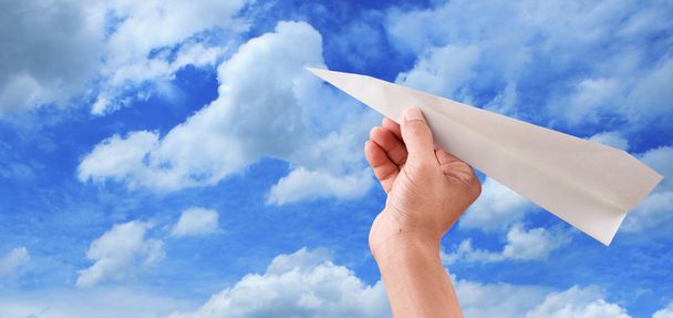 Рука бросает бумажный самолет к голубому небу
 - Фото, изображение