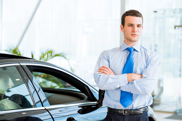 dealer stands near a new car in the showroom - Foto, imagen