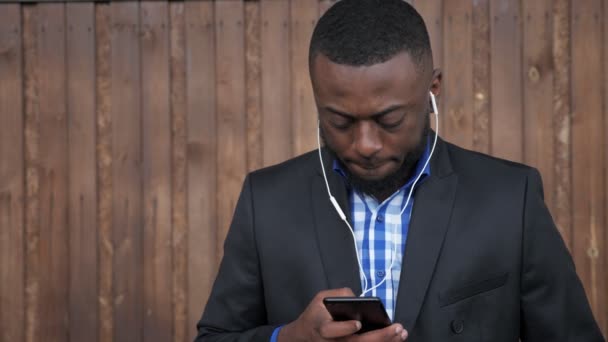 Homme noir dans les écouteurs navigue téléphone mobile sur fond de bois sombre
. - Séquence, vidéo
