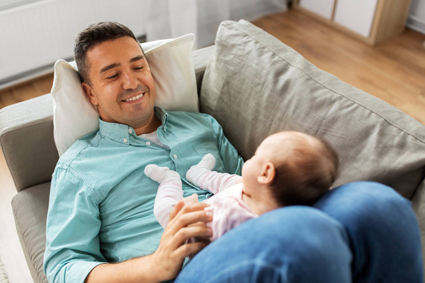 middle aged father with baby lying on sofa at home - 写真・画像
