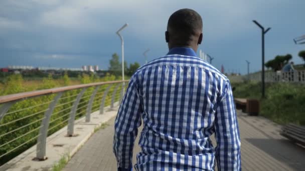 Νέος Αφρο-Αμερικανός άνθρωπος περπατάει στο πάρκο της πόλης σε συννεφιασμένη καλοκαιρινή μέρα. - Πλάνα, βίντεο
