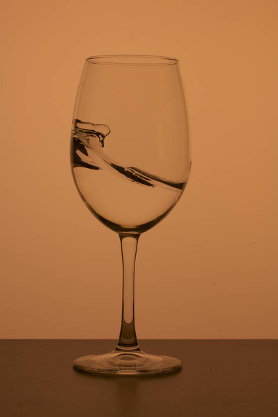 Wine glass on a long stem. A little drink is poured into it, a splash is visible. In back yellow color. - Foto, immagini