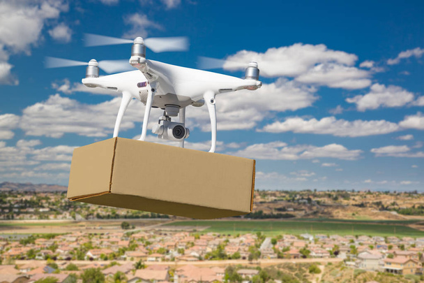 Sistema de aviones no tripulados (UAS) Drone Quadcopter que lleva el paquete en blanco sobre el vecindario
 - Foto, Imagen