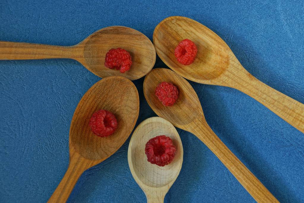 Conjunto de cucharas marrones de madera con bayas rojas de frambuesa sobre una mesa azul
 - Foto, Imagen