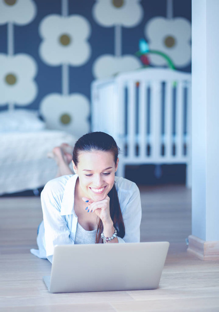 Young woman sitting on the floor near childrens cot with laptop. Young mom - Foto, Bild