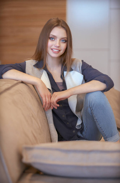 Woman sitting on her white sofa in white pullover - Fotoğraf, Görsel