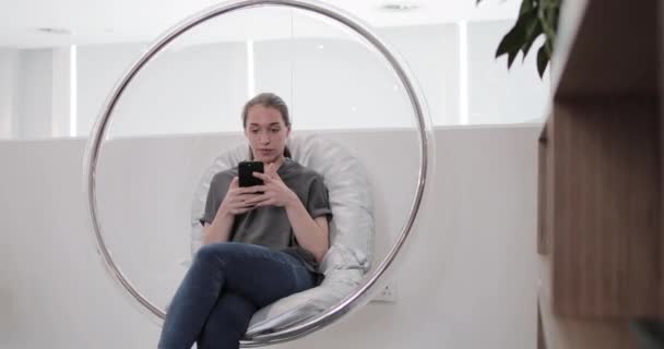 Hispanic businesswoman using smartphone in an egg chair - Materiał filmowy, wideo
