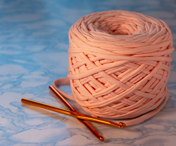 A coil of large knitted yarn of peach color with two orange shiny hooks on the surface of blue marble - Photo, image