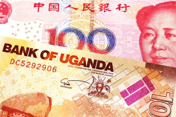 Un billet rouge de cent yuans en provenance de Chine avec un billet de mille shillings ougandais en gros plan en macro
 - Photo, image
