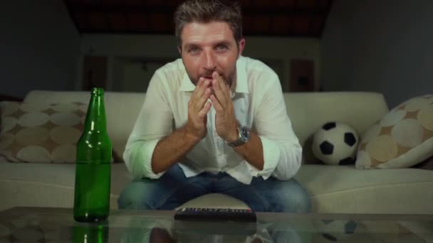 young attractive excited and stressed soccer fan man gesturing nervous at home couch with beer bottle watching television football match spastic on living room sofa feeling the stress and emotion of competition - Filmmaterial, Video