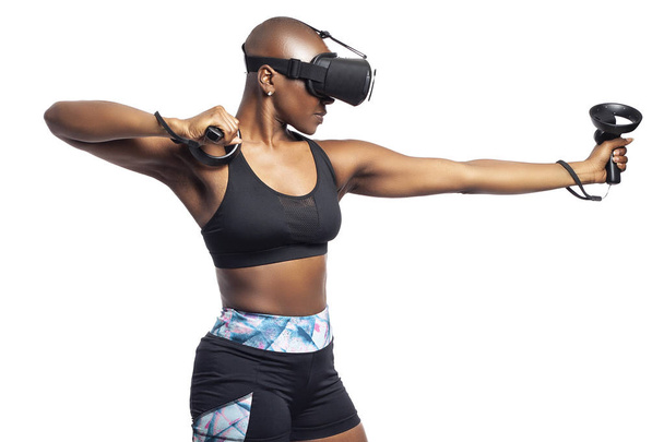 Musta nainen yllään virtuaalitodellisuus kuulokkeet teeskentelee tehdä keula ja pelaa VR jousiammunta videopeli. Hän tähtää kohteeseen. Riippuvuudet urheilusta
.  - Valokuva, kuva