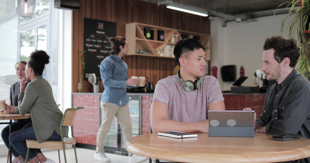Ελεύθεροι επαγγελματίες σε μια συνάντηση σε ένα καφέ κοιτάζοντας μια ψηφιακή ταμπλέτα - Πλάνα, βίντεο