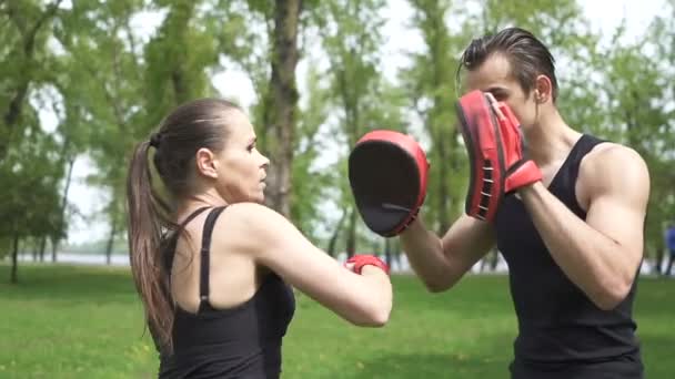 スローモーション。屋外の都市公園エリアで女性と男性のトレーニングボクシングプロセス。安定したショット - 映像、動画