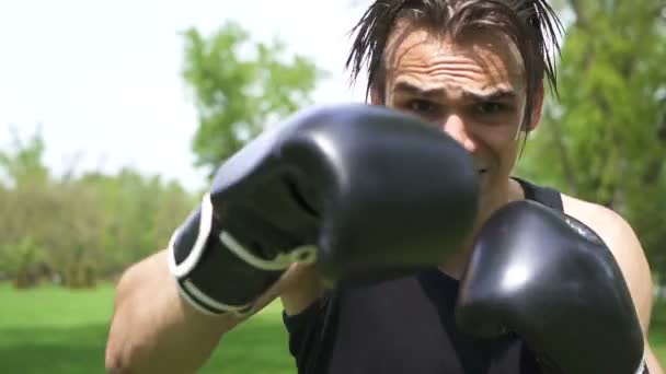 Zwolnionym. Młody muskularny bokser w czarnych rękawiczkach robi ciosy w aparacie. Stabilny strzał  - Materiał filmowy, wideo