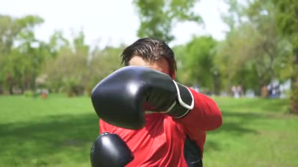 Au ralenti. Jeune boxeur homme musclé en gants noirs fait des coups à la caméra directe. Tir stabilisé
 - Séquence, vidéo