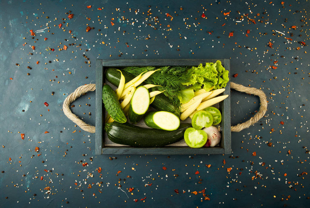 FRESH VEGETABLES ON WOODEN BOX ON A DARK STONE BACKGROUND. THE CONCEPT OF VINTAGE. THE YOUNG CORN ONIONS ASPARAGUS GREEN TOMATO CUCUMBER ON A DARK SURFACE. - Photo, Image