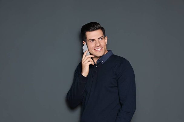 Portrait of handsome man talking on phone against grey background - Fotografie, Obrázek