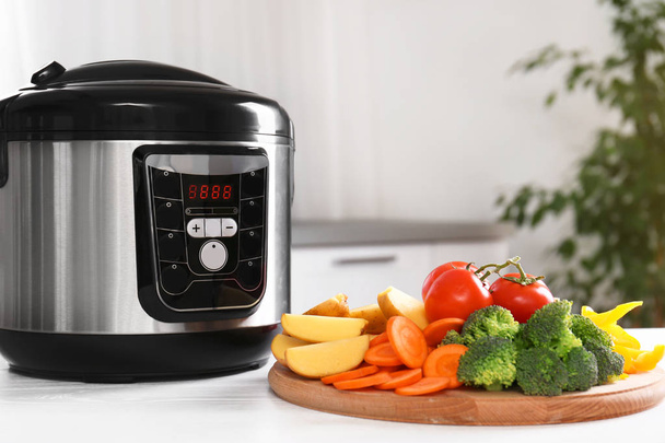 Modern multi cooker and wooden board with vegetables on white table indoors - Foto, afbeelding
