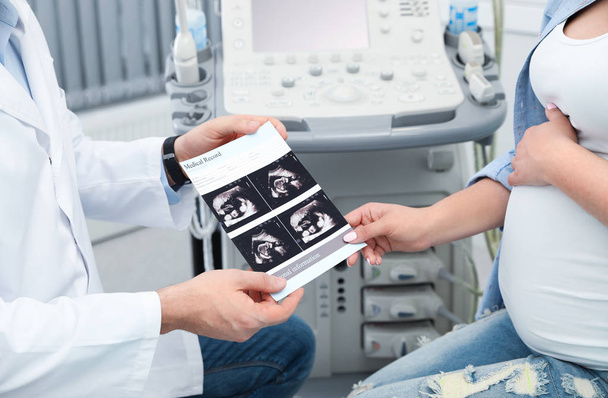 Doctor showing ultrasound images of baby to future mother in clinic, closeup - Photo, Image