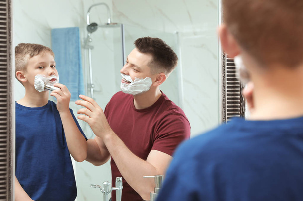 Dad teaching his son to apply shaving foam on face at mirror - Фото, изображение