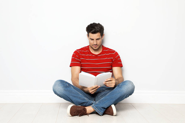 Handsome man reading book on floor near white wall - Zdjęcie, obraz